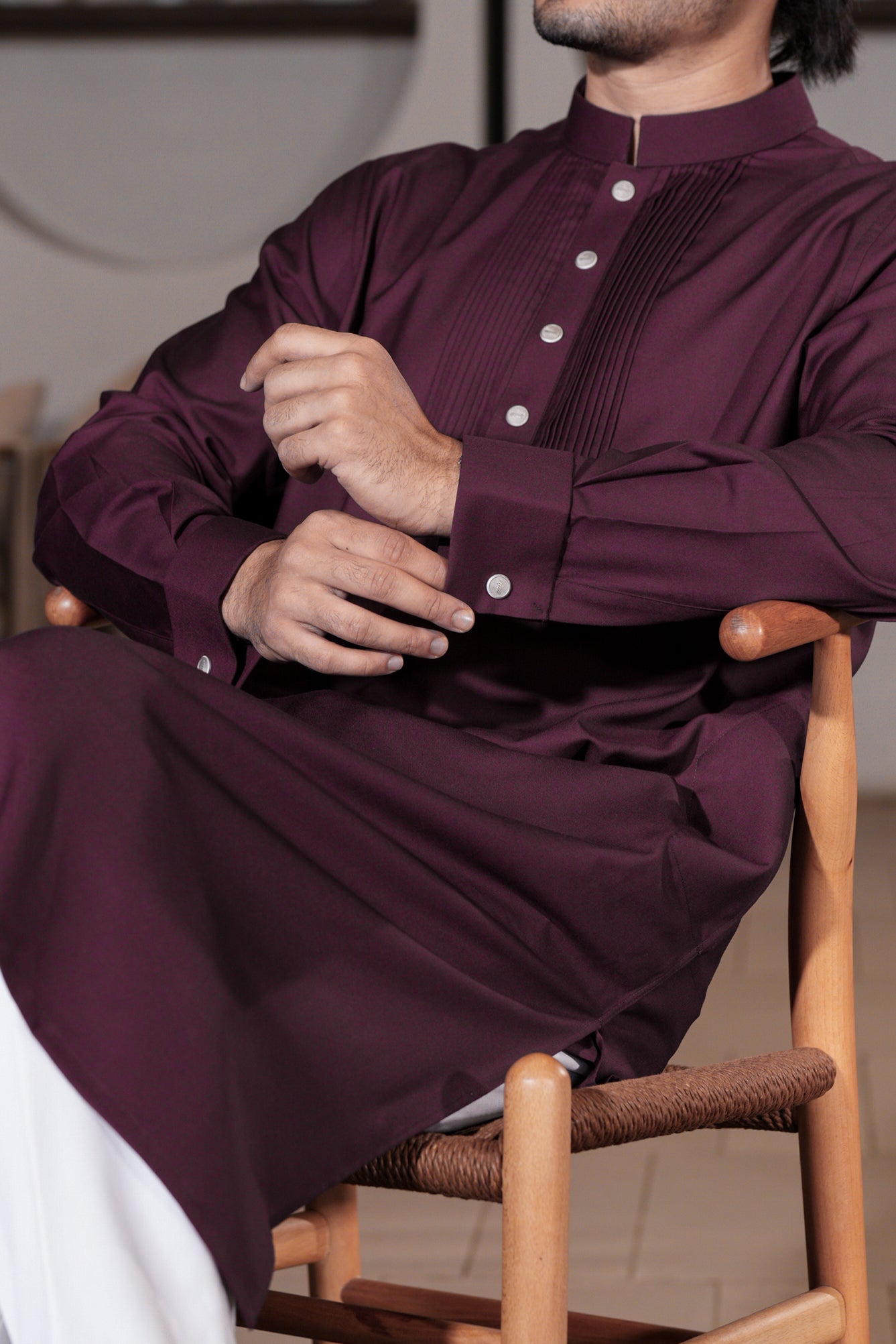 Person wearing a dark purple traditional outfit sitting on a wooden chair.