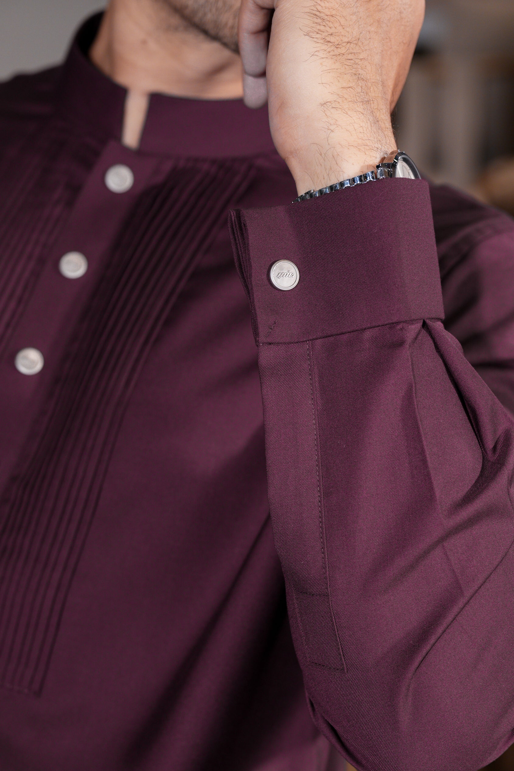 Close-up of a maroon shirt with buttons and a cuff, blurred background