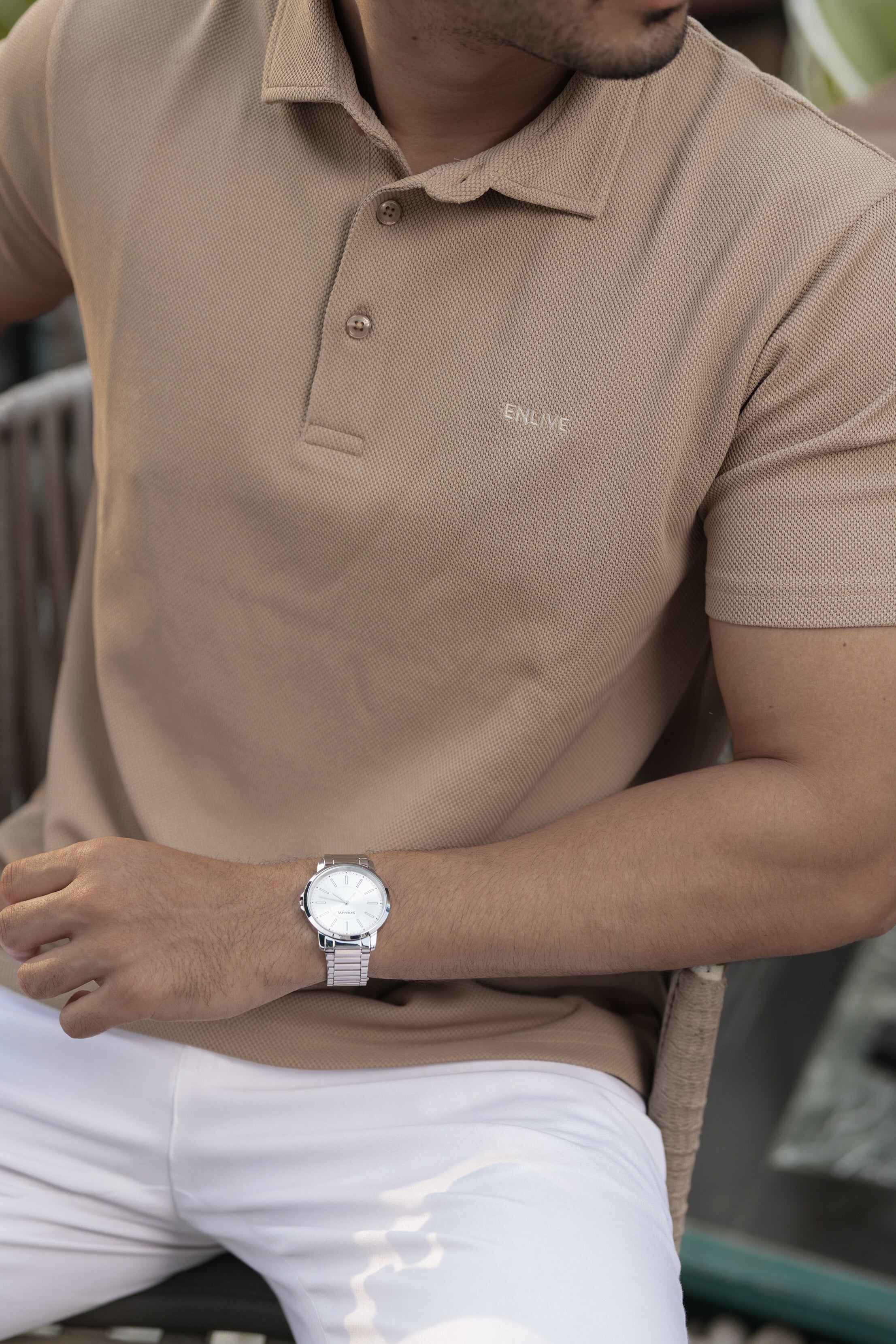 Man wearing a beige polo shirt and white pants with a watch on his wrist.