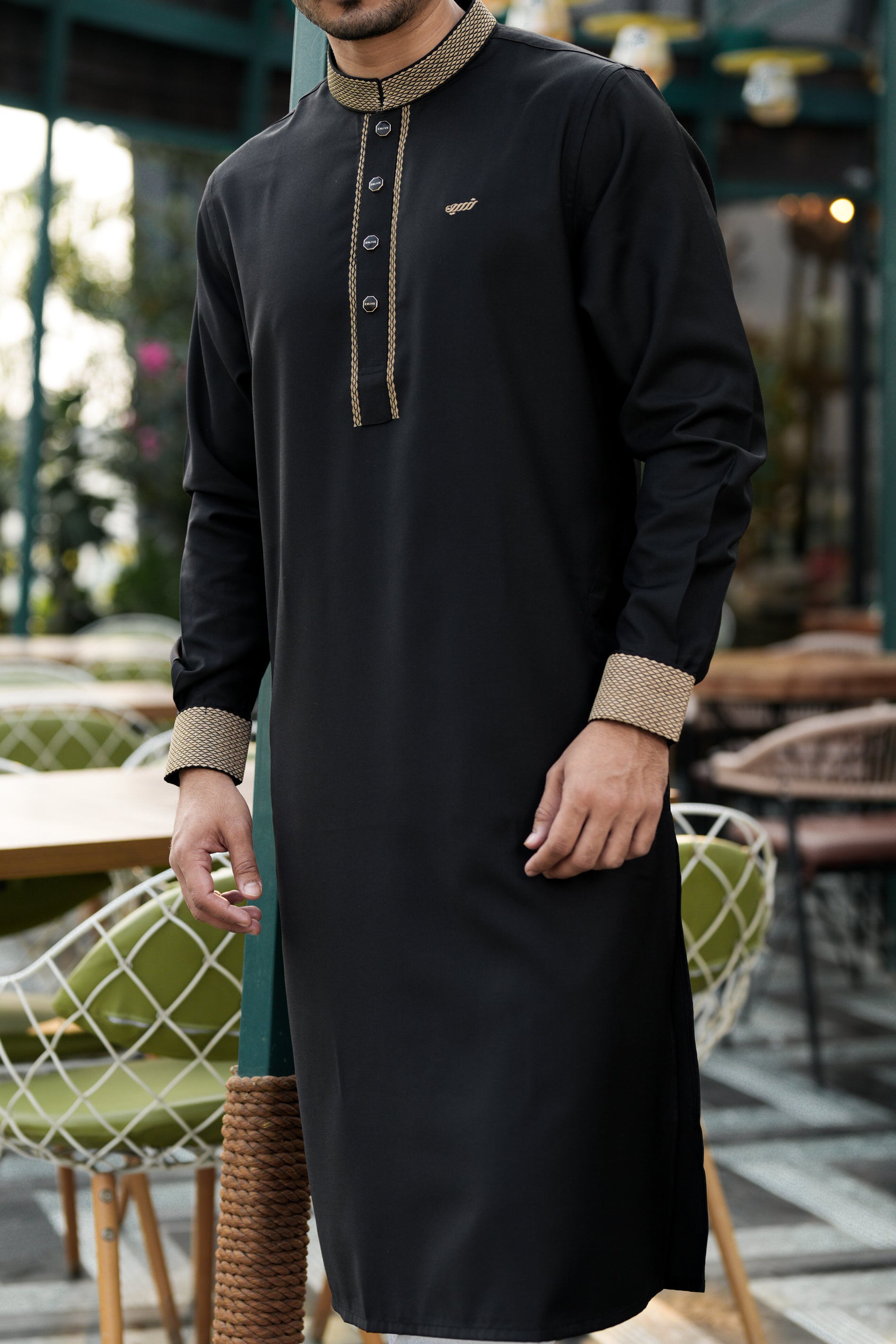 Person wearing a black traditional outfit with beige accents in an outdoor setting.