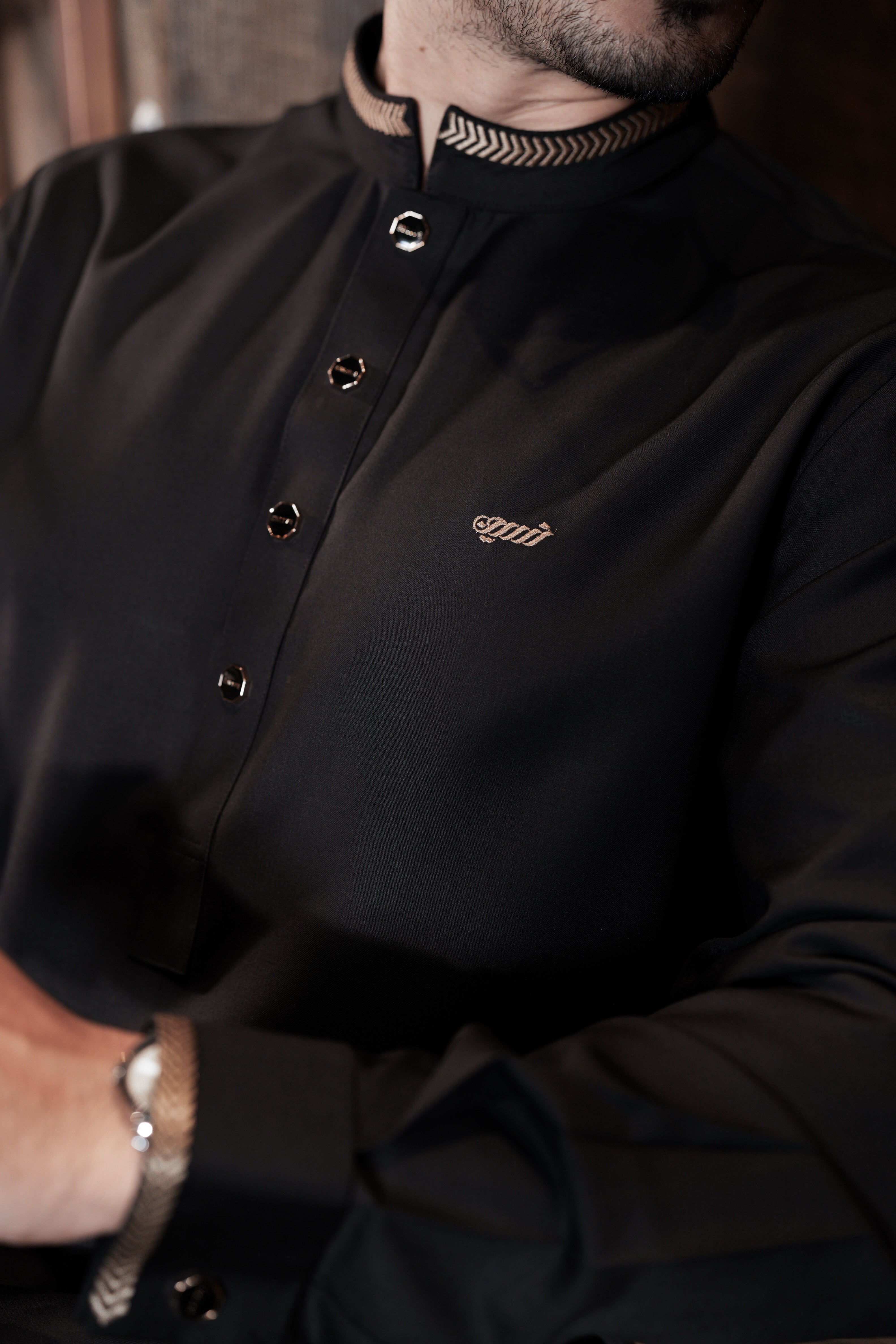 Close-up of a person wearing a black jacket with a brand logo, sitting indoors.