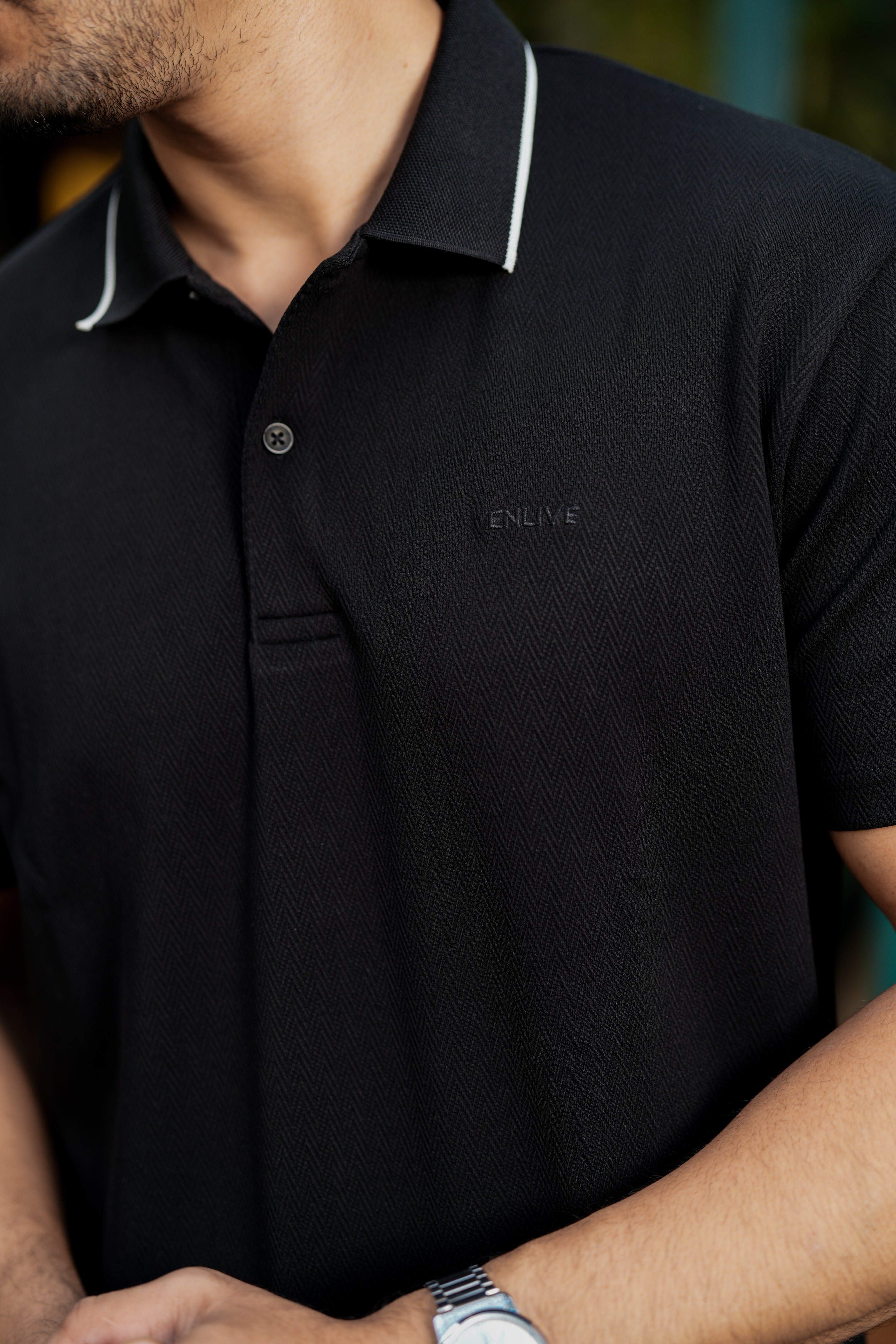 Black polo shirt with white trim worn by a person, brand logo visible.