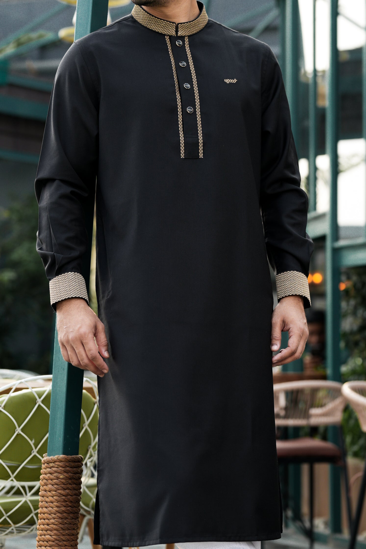 Person wearing a black traditional outfit with beige accents in an outdoor setting.