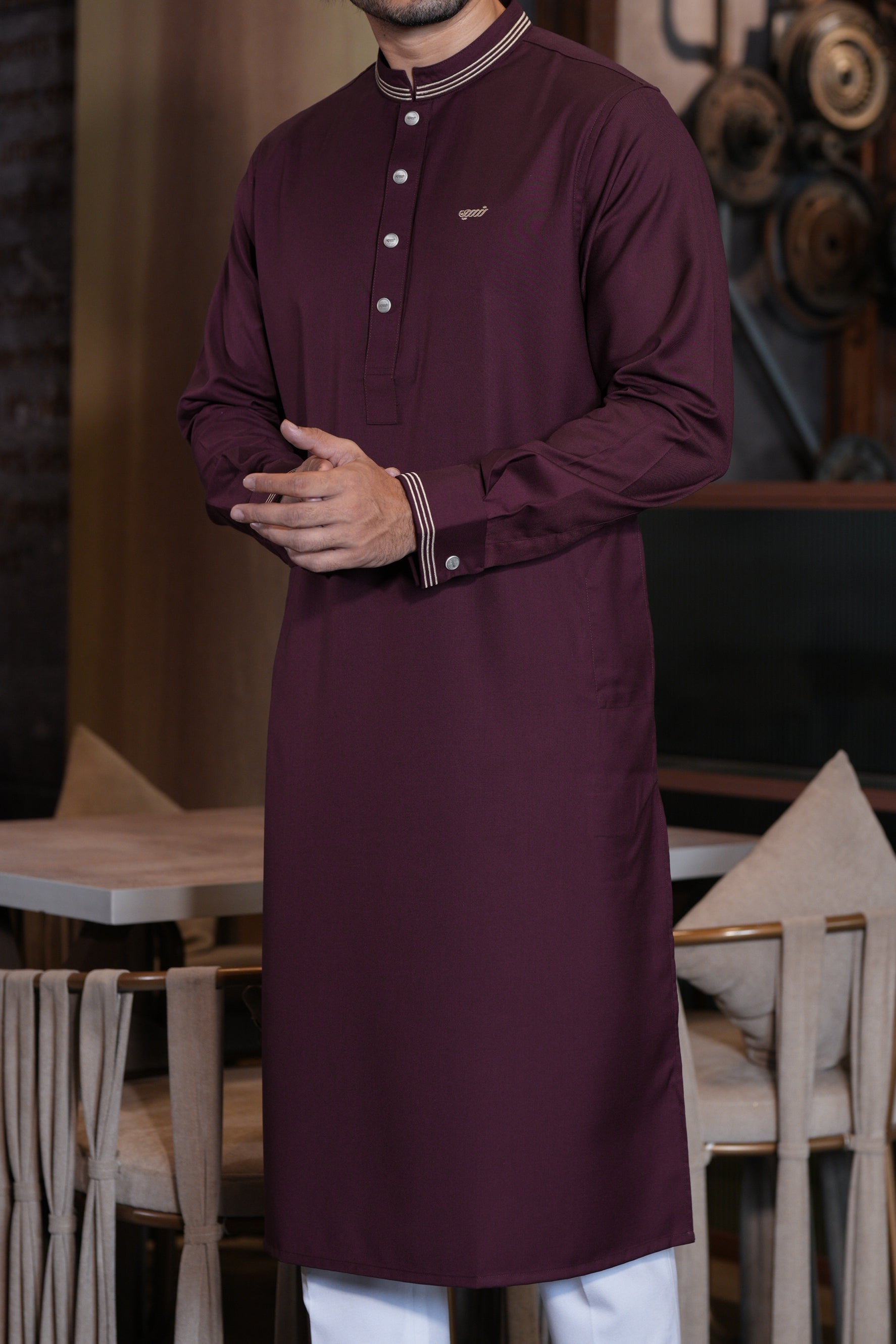 Man wearing a long, dark purple traditional outfit with white buttons in an indoor setting.