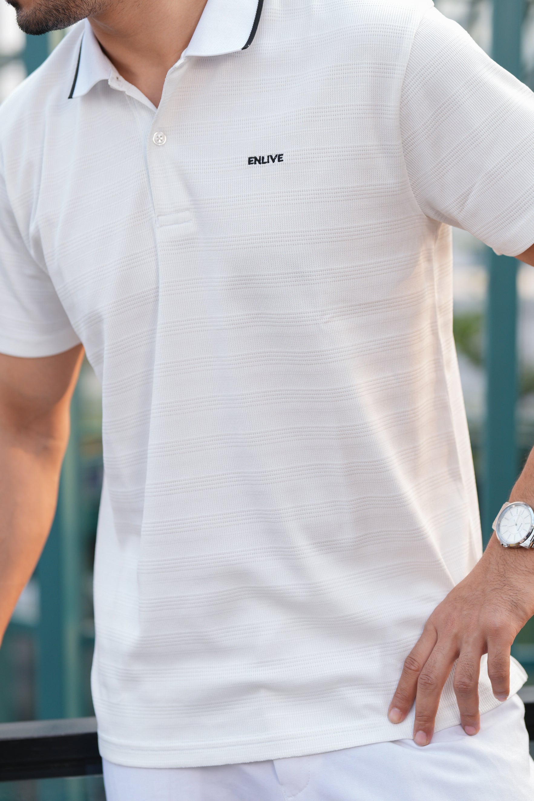 Man wearing a white polo shirt with a brand logo, standing outdoors.