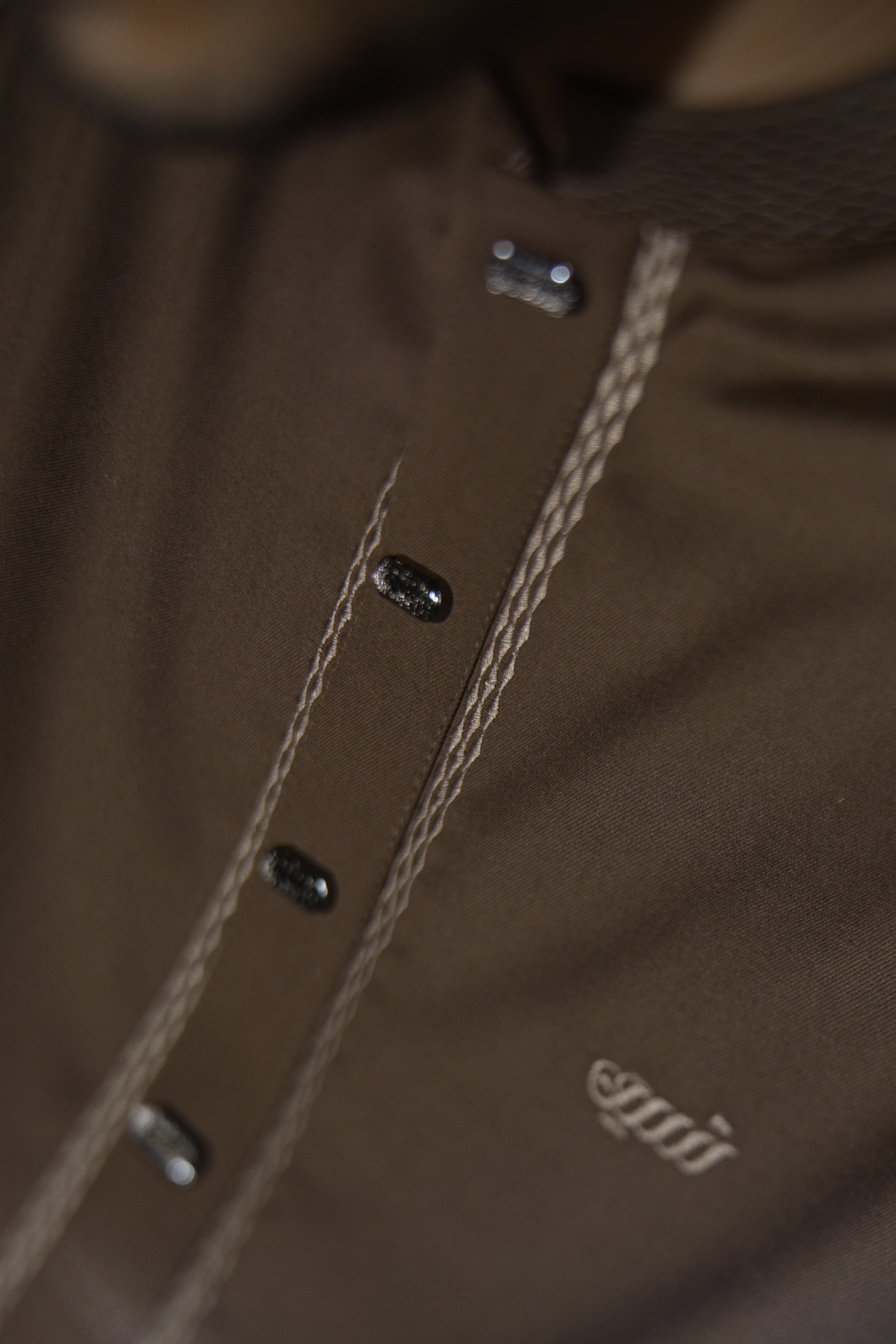 Close-up of a brown jacket with buttons and a brand logo.