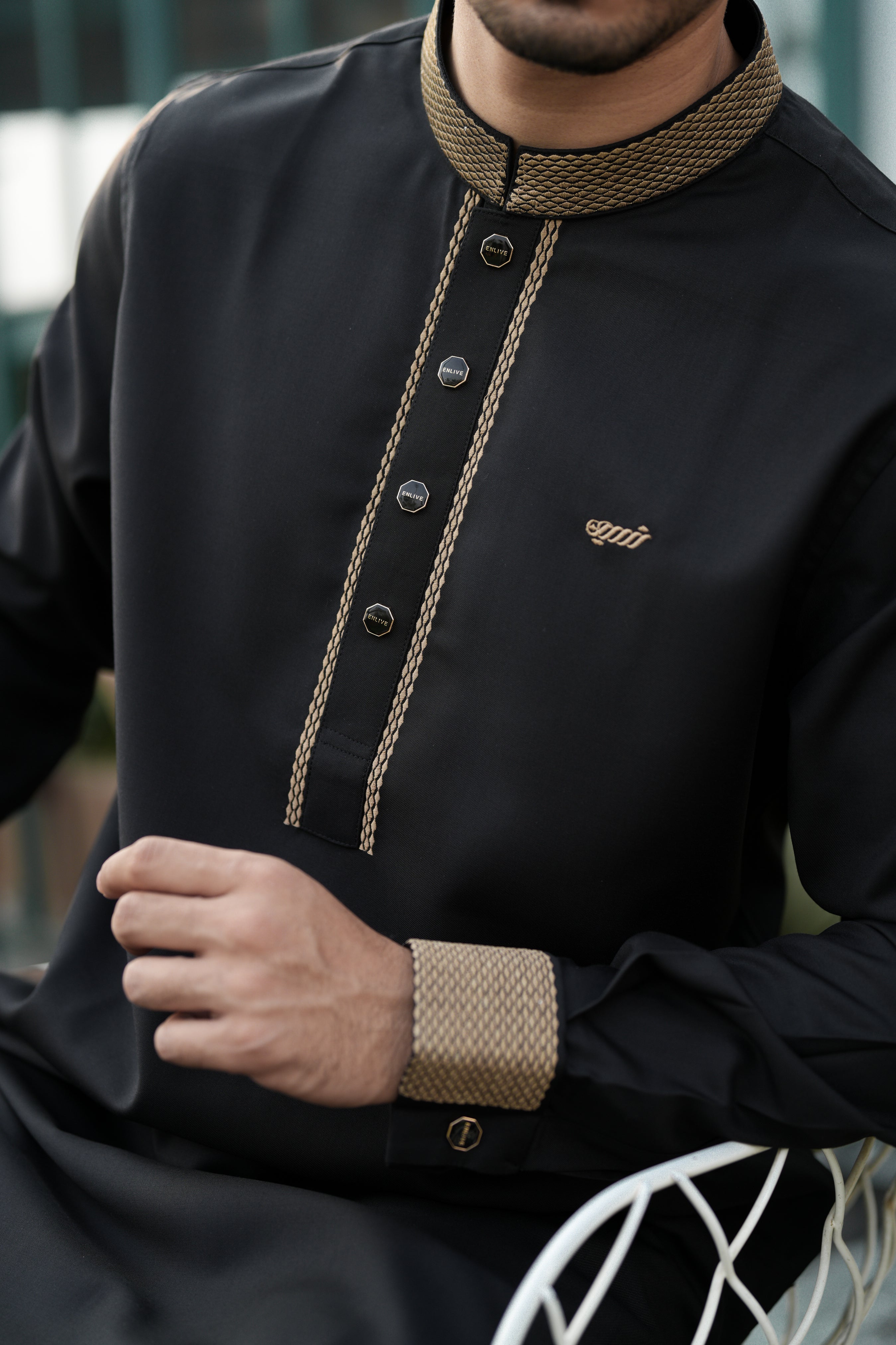 Man wearing a black outfit with gold accents, sitting outdoors.