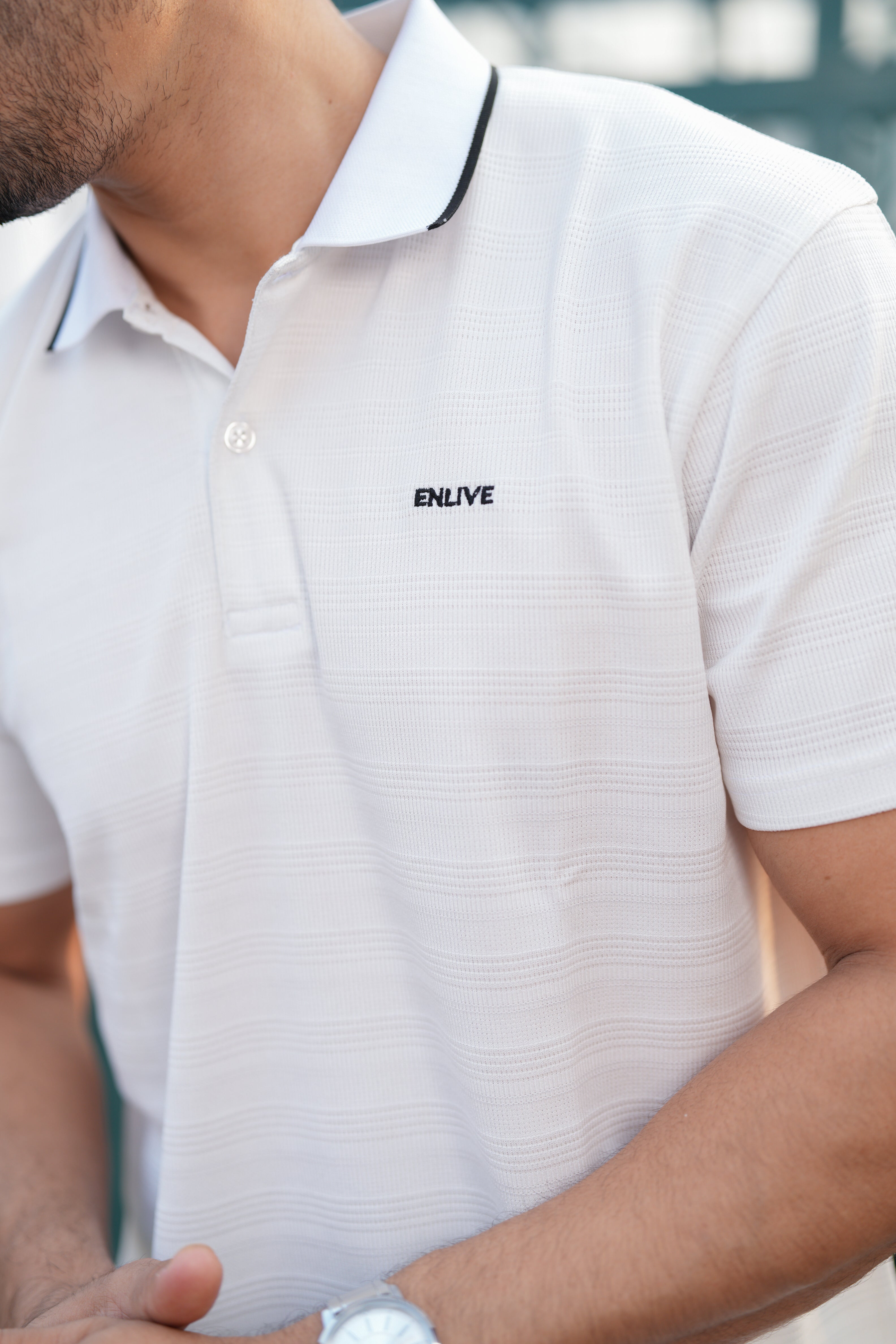 White polo shirt with 'ENLIVE' logo on a blurred background