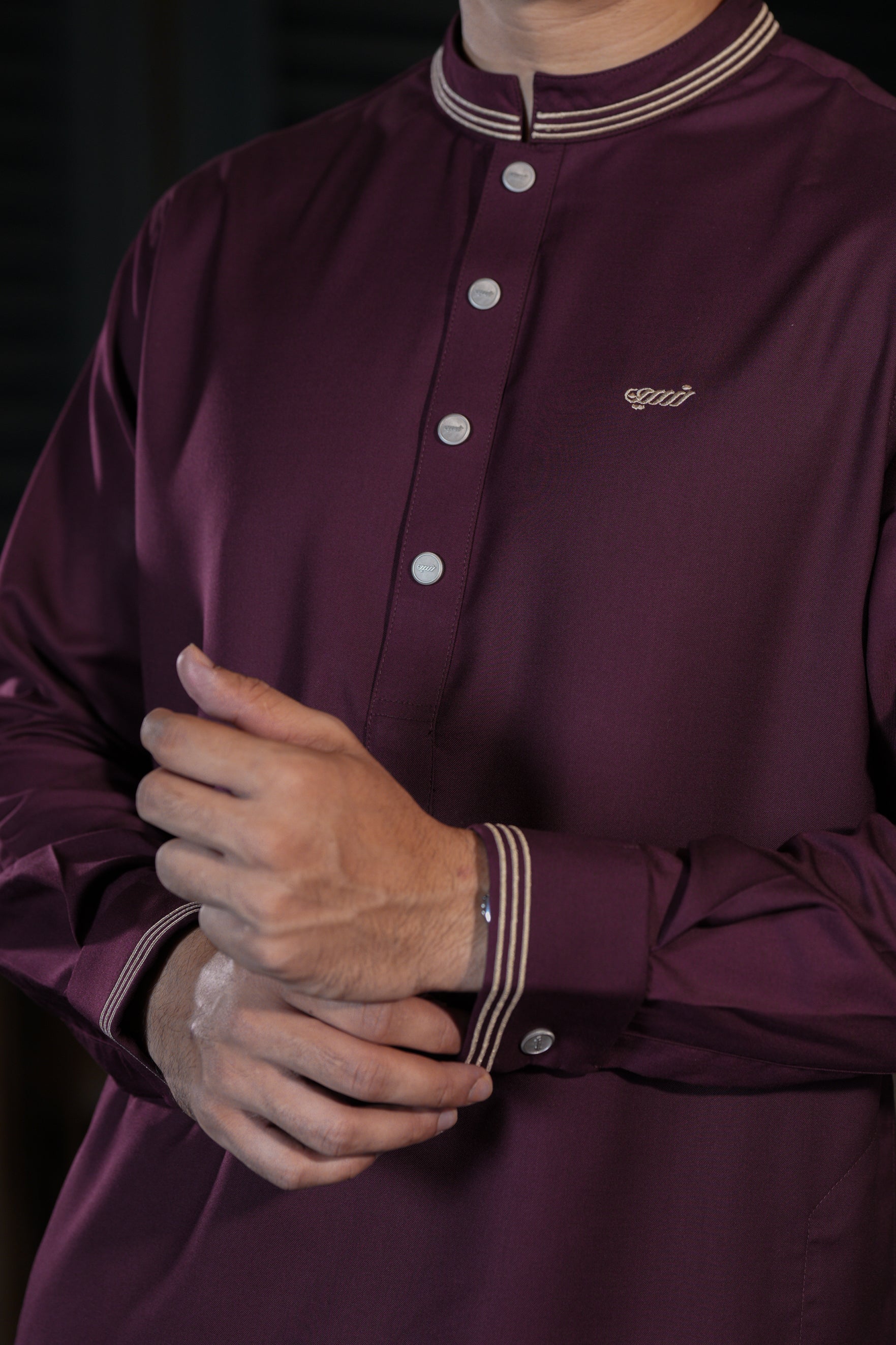Close-up of a person wearing a maroon shirt with a brand logo on a dark background