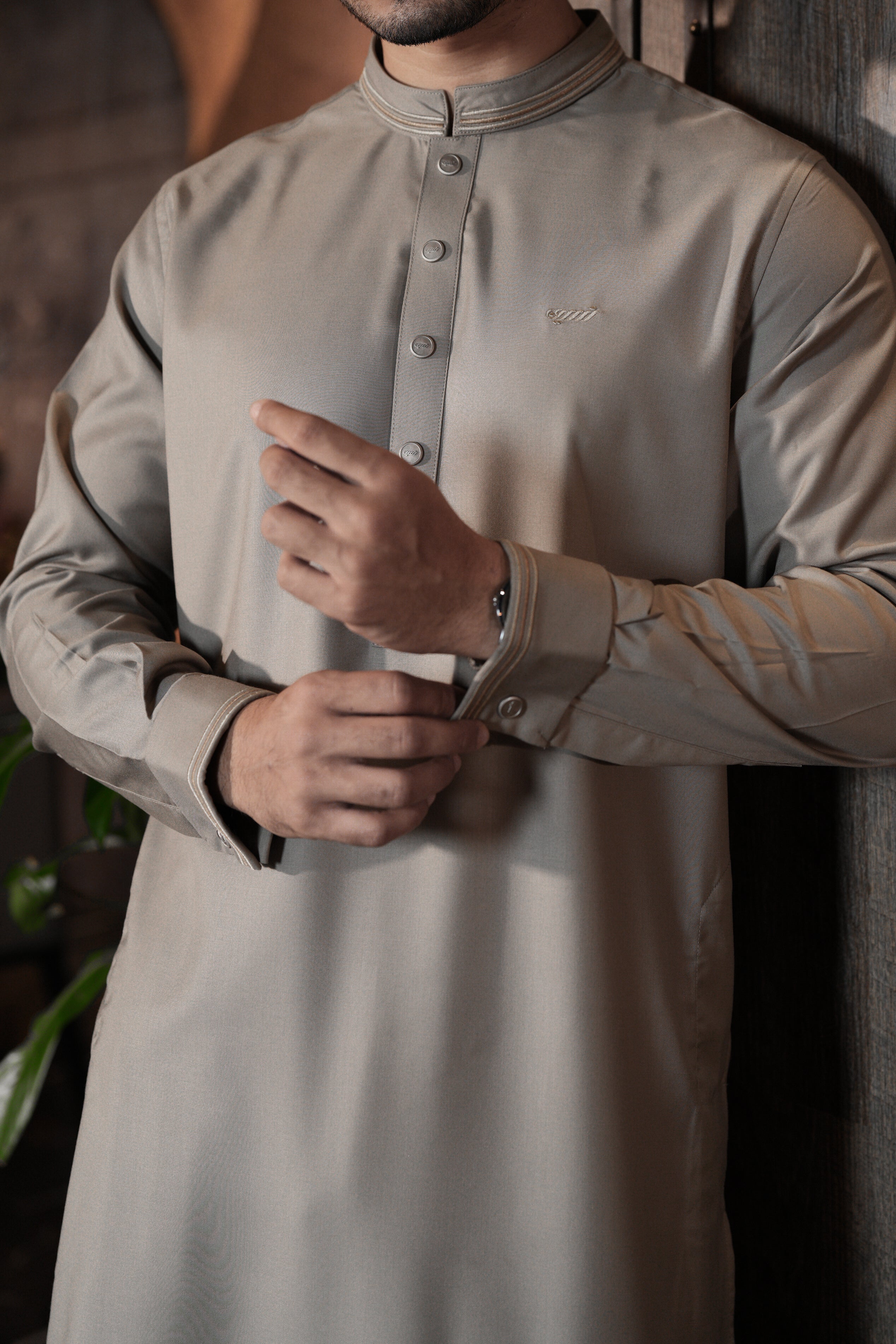 Man wearing a light gray traditional outfit with a subtle brand logo.