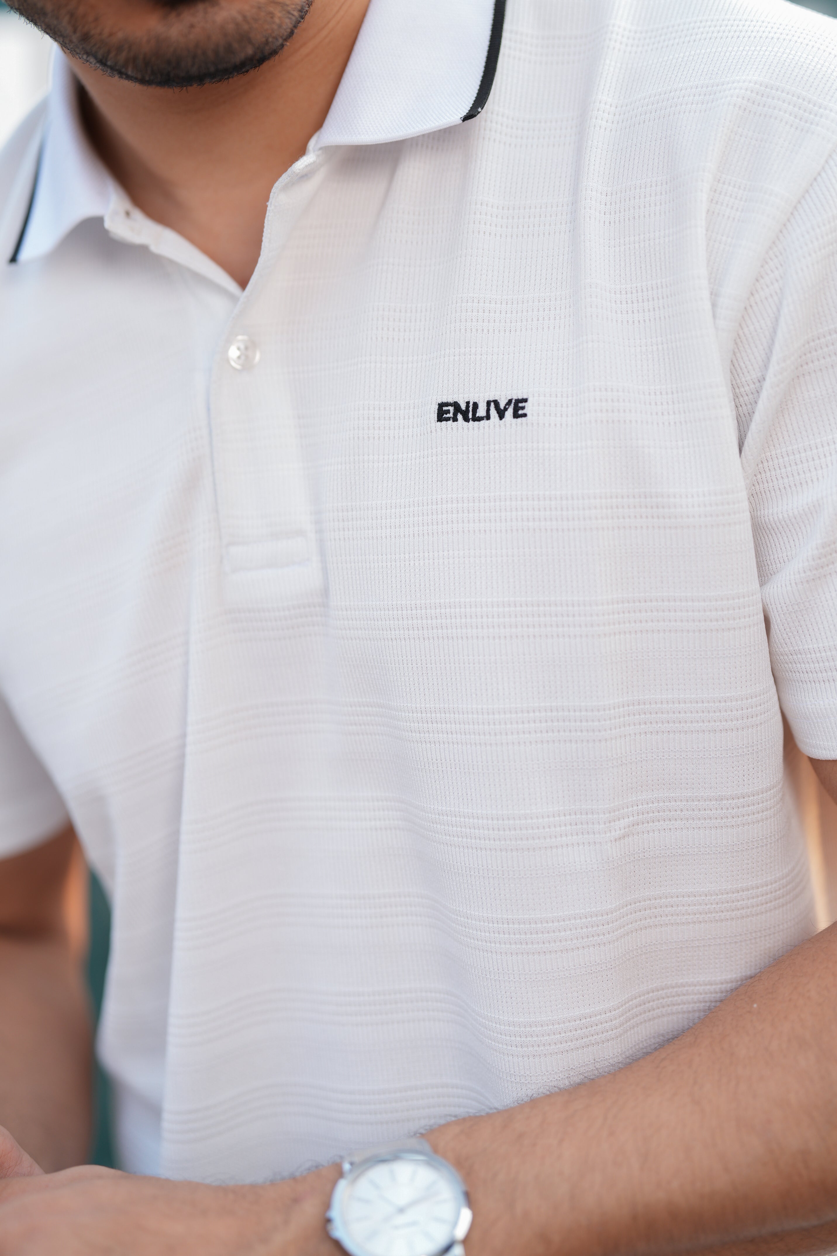 White polo shirt with 'ENLIVE' logo worn by a person, close-up view.