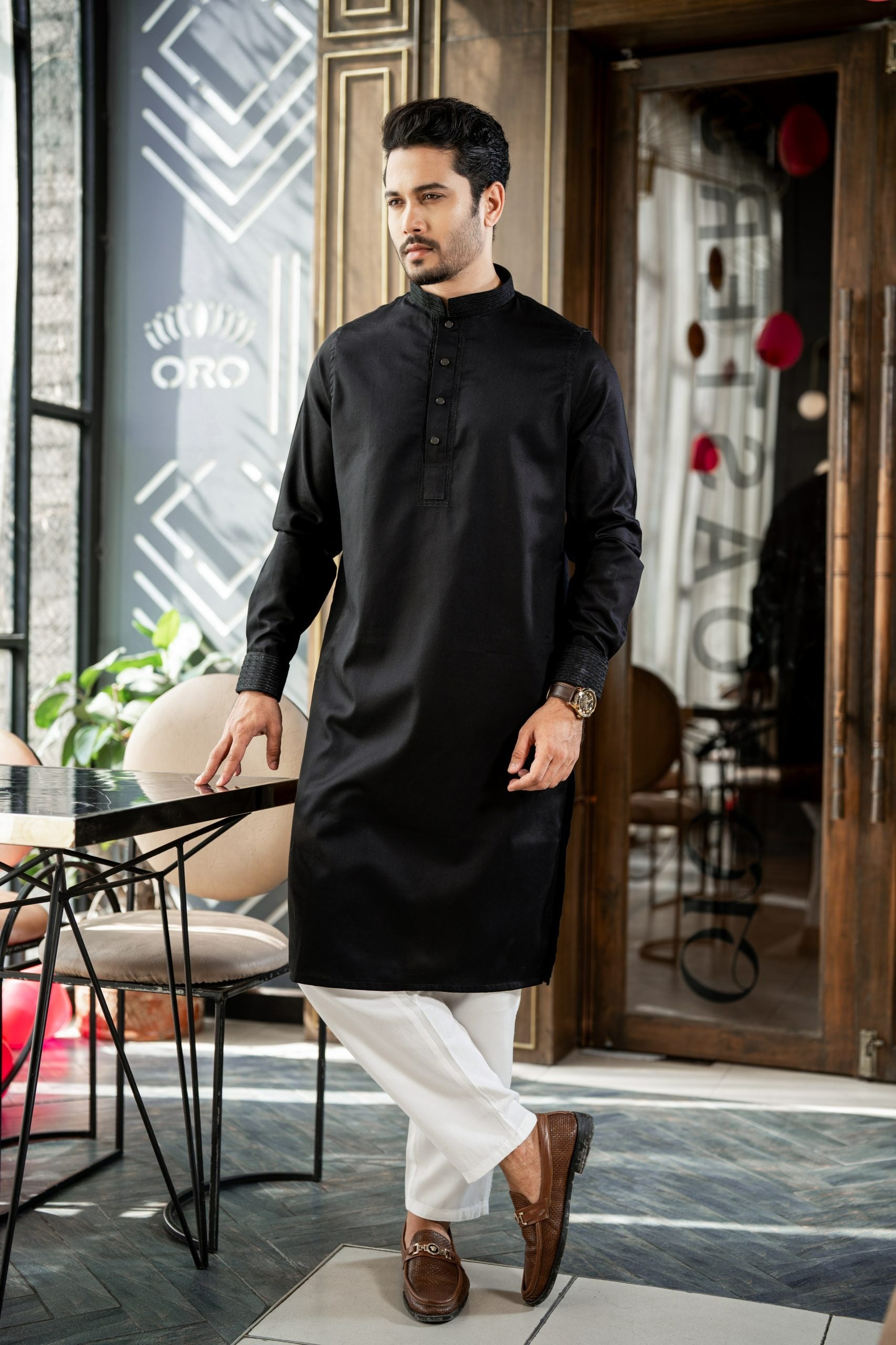 Man wearing a black kurta with white pants in an indoor setting