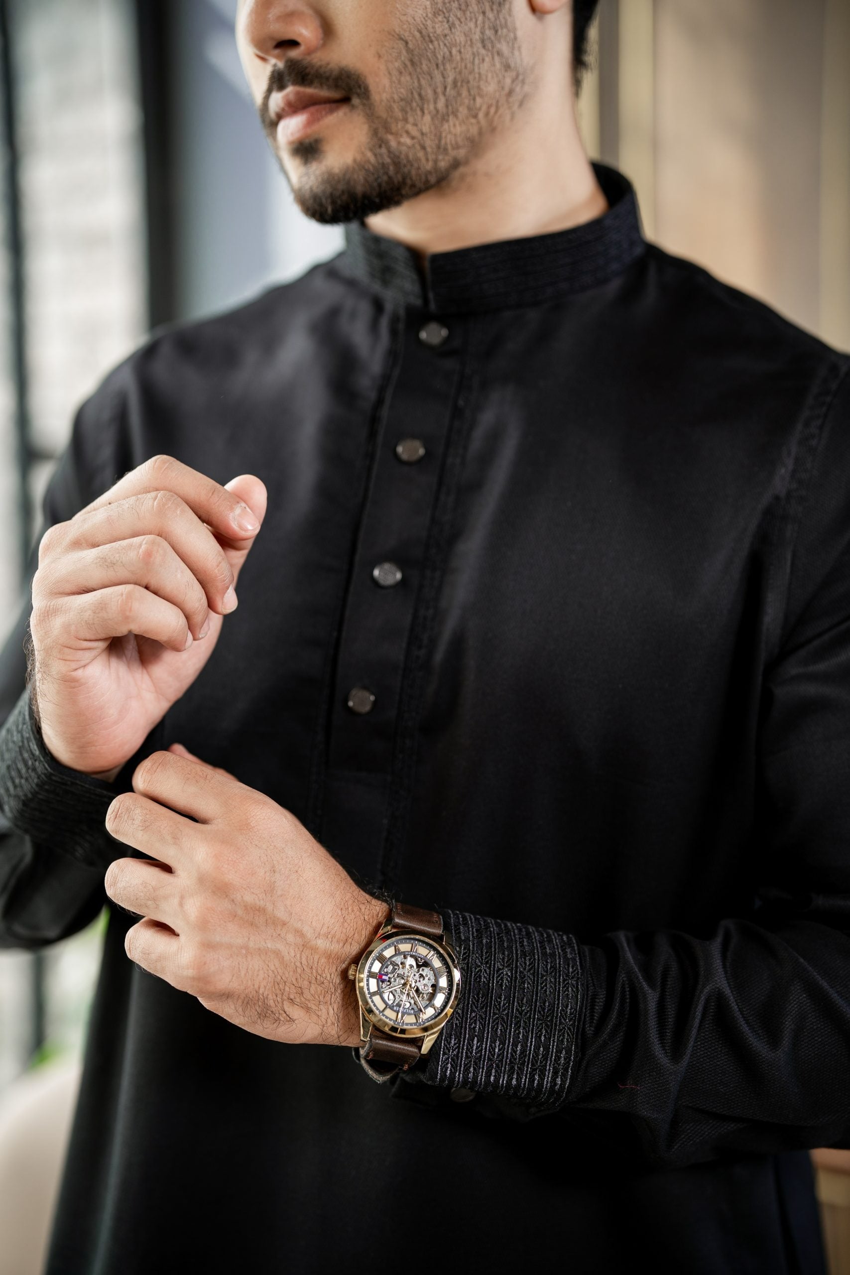 Man wearing a black traditional outfit with a watch on his wrist.