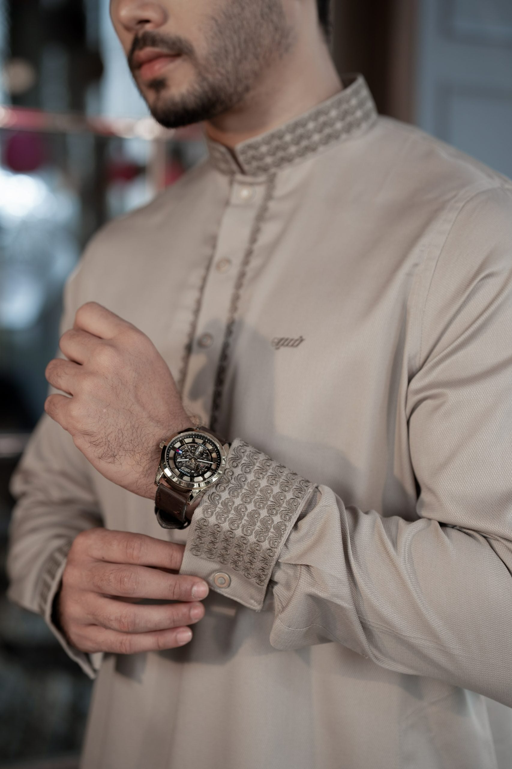 Man wearing a beige traditional outfit with a watch on his wrist.