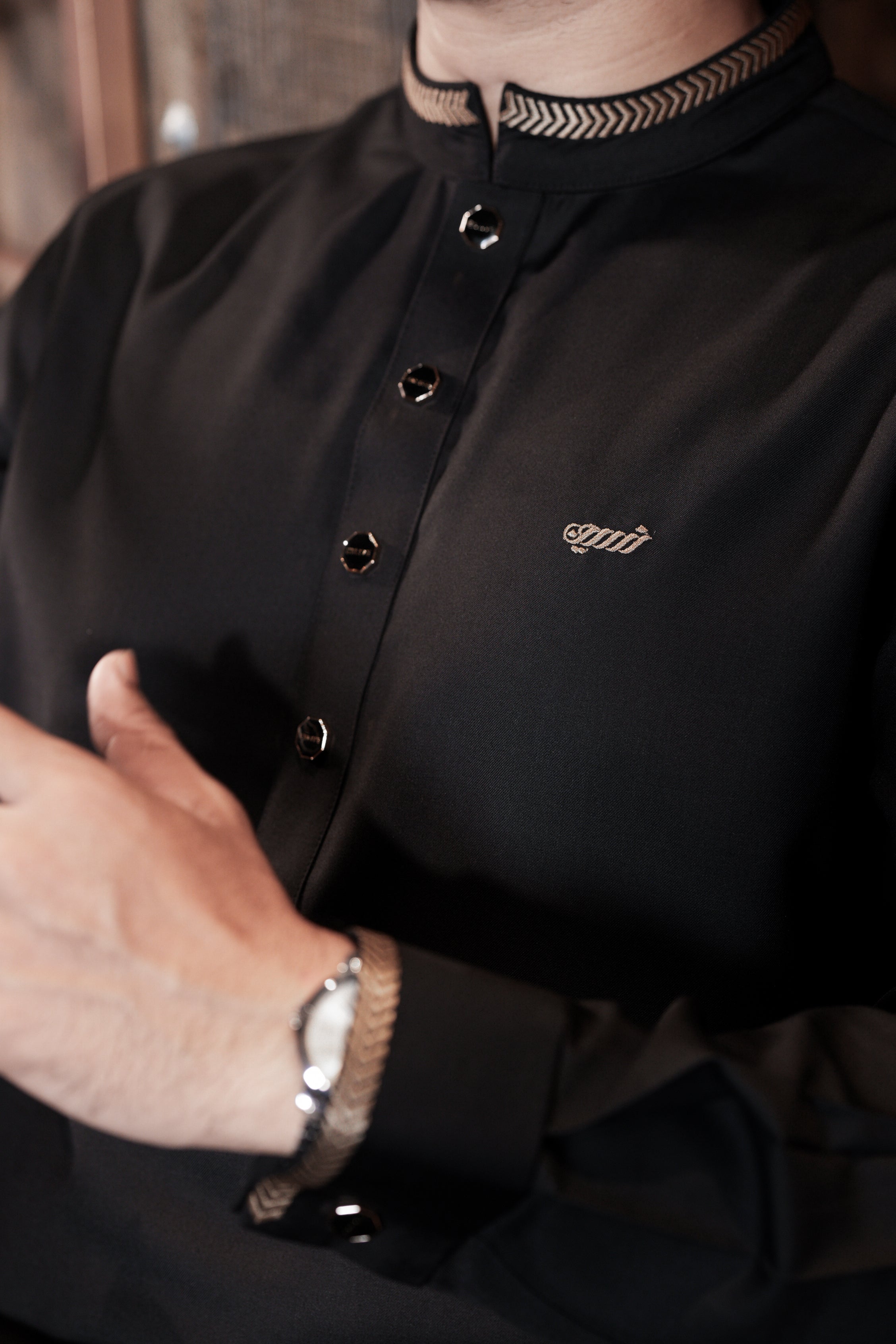 Close-up of a person wearing a black shirt with a brand logo, focusing on the collar and chest area.