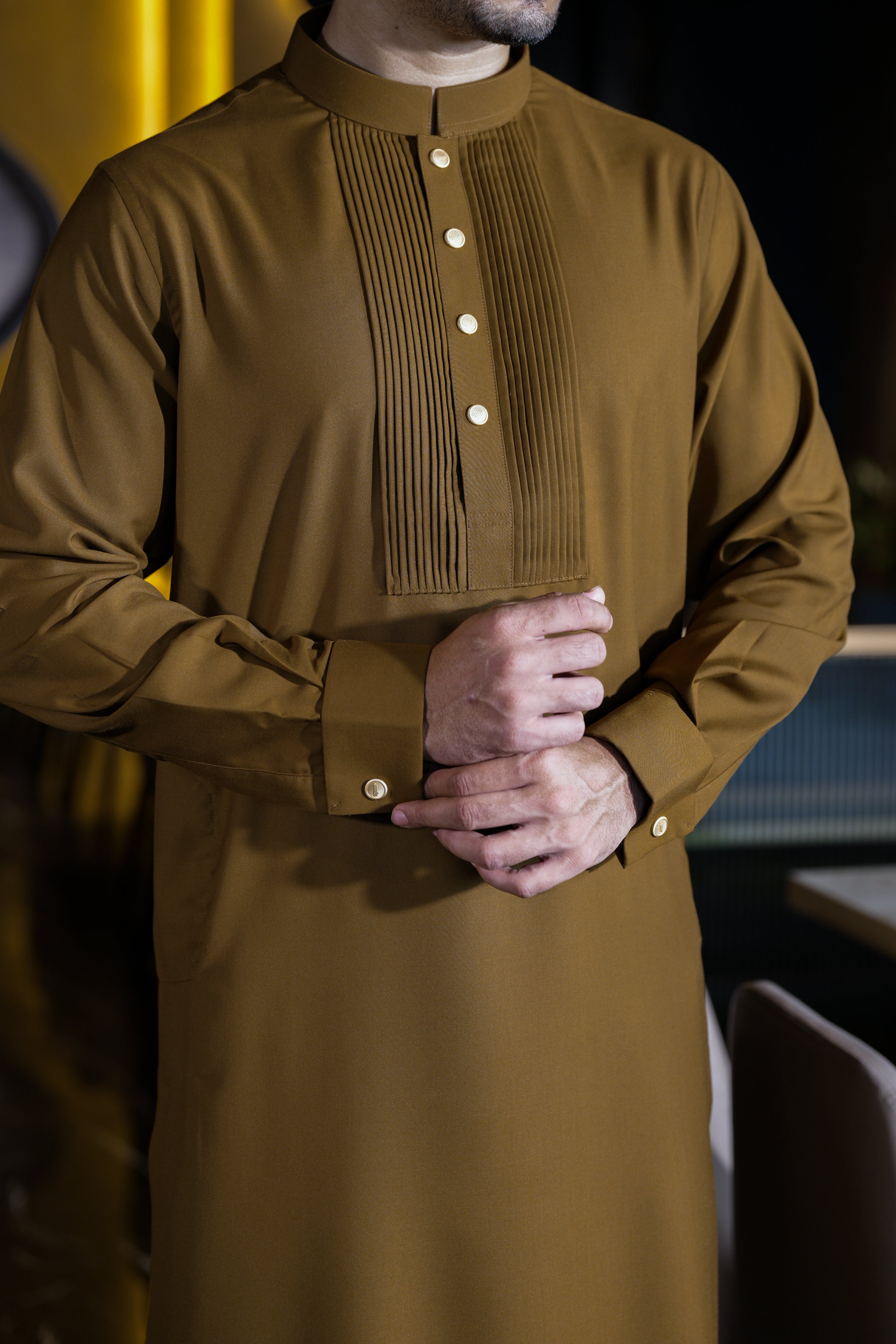 Man wearing a brown traditional outfit with pleated details.