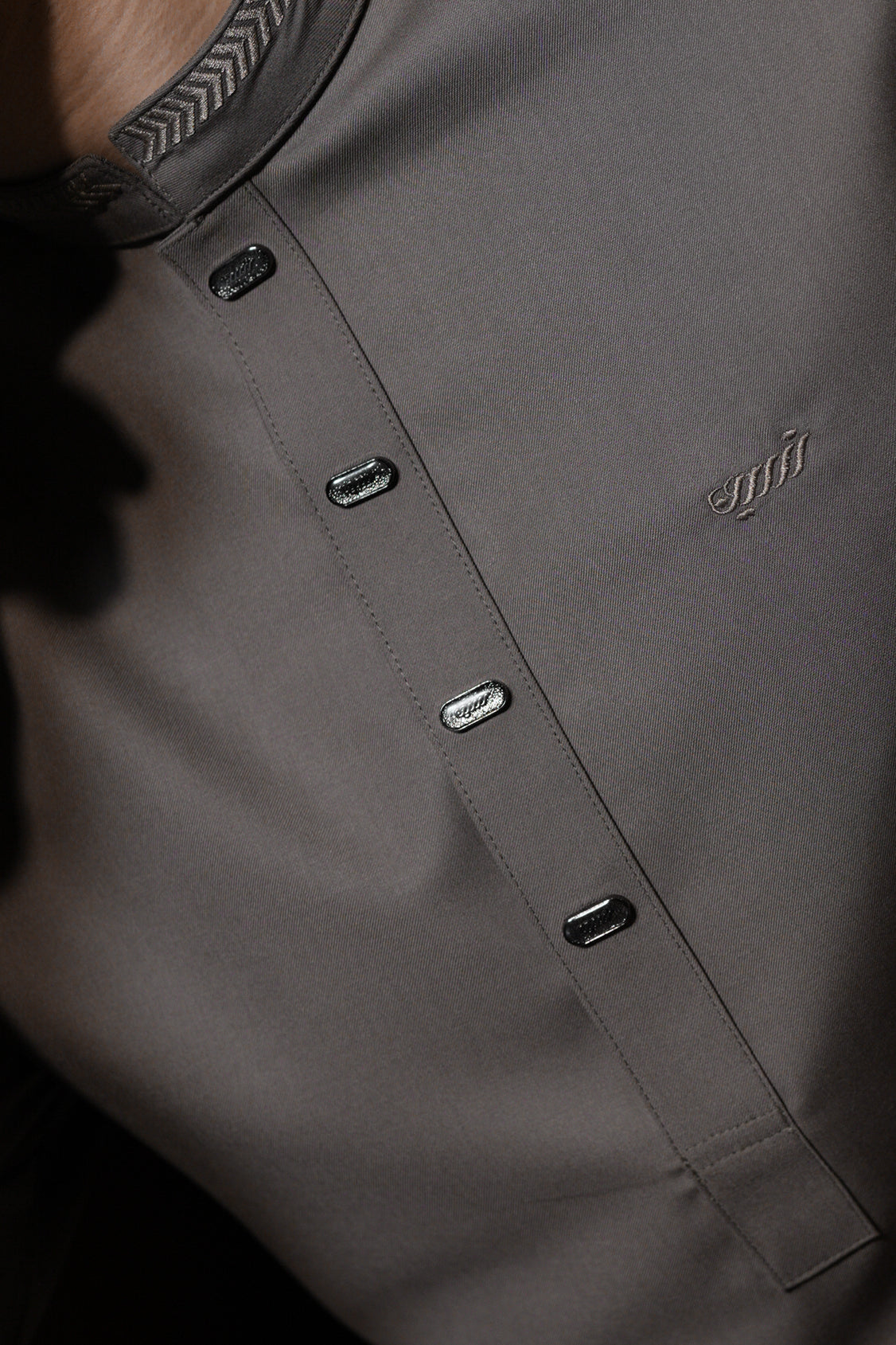 Close-up of a gray shirt with buttons and a brand logo.