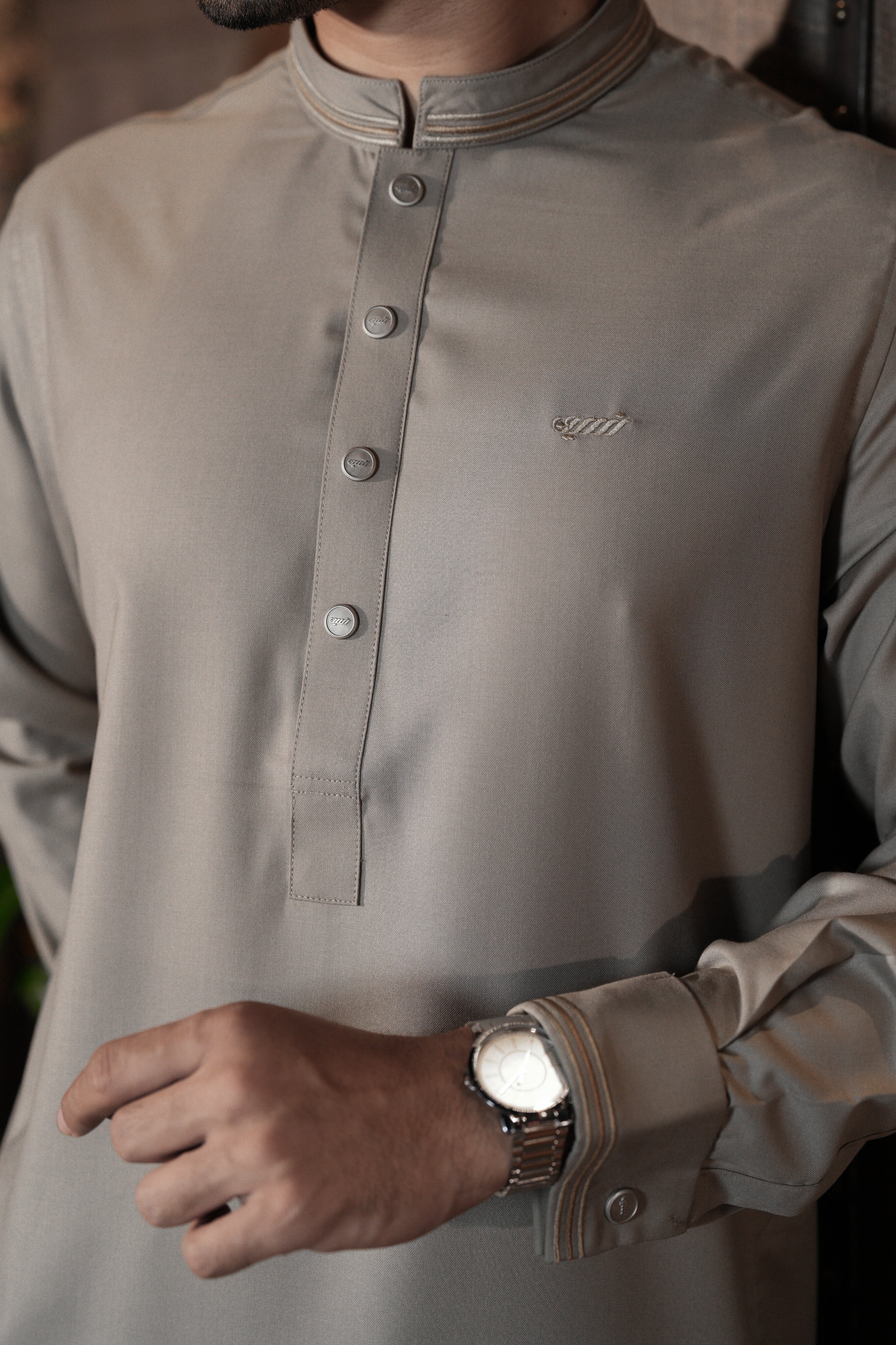 Close-up of a person wearing a beige long-sleeve shirt with a brand logo, focusing on the chest area.