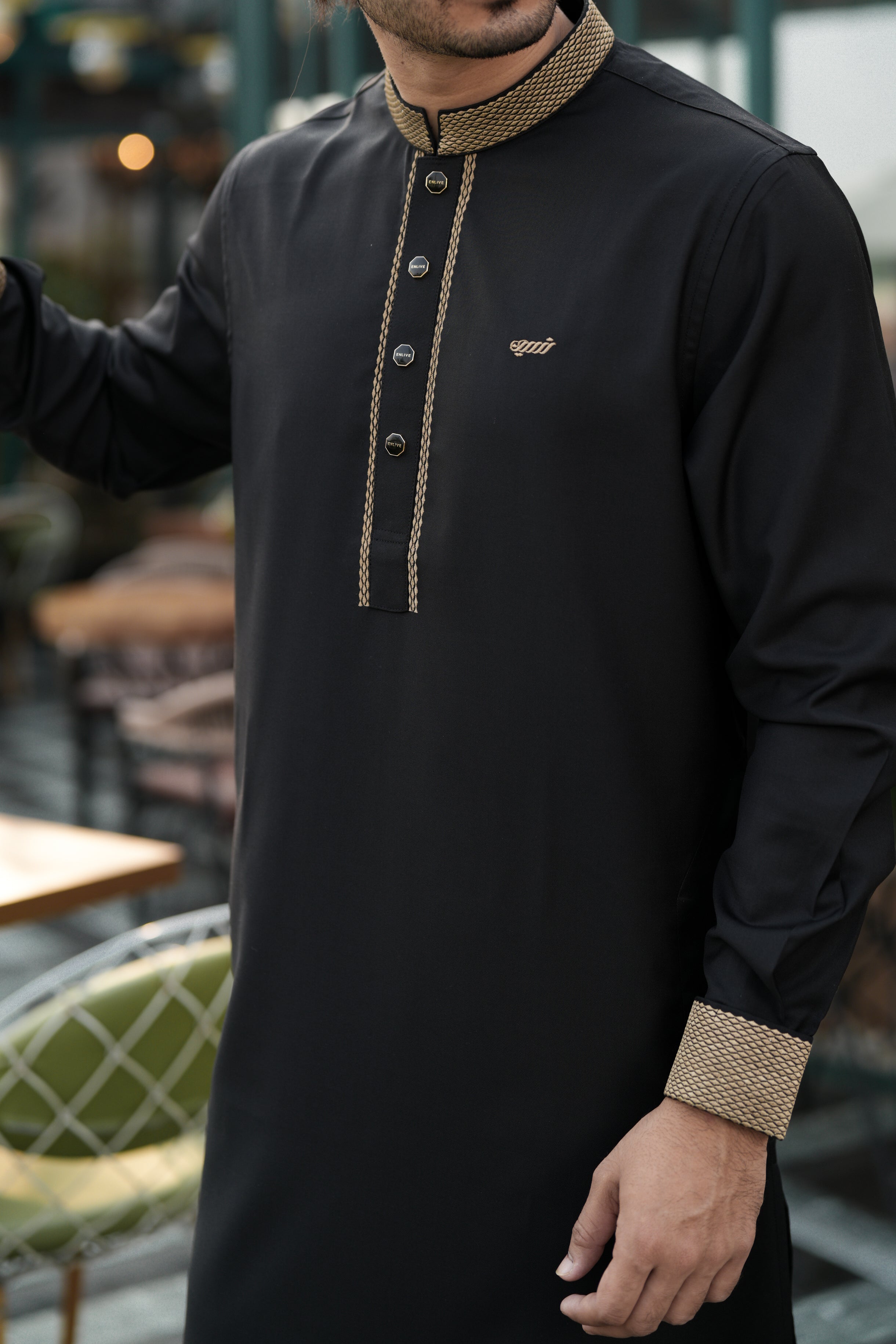 Man wearing a black traditional outfit with beige details outdoors.