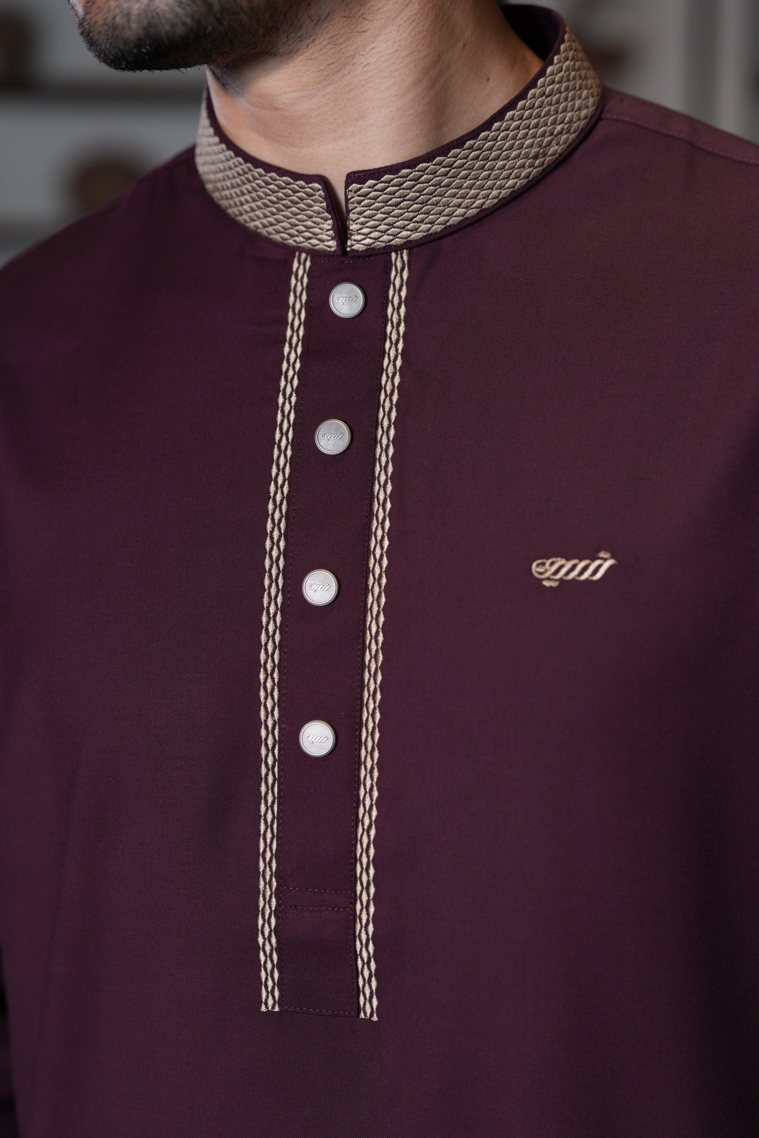 Close-up of a maroon shirt with embroidered collar and buttons, featuring a brand logo.