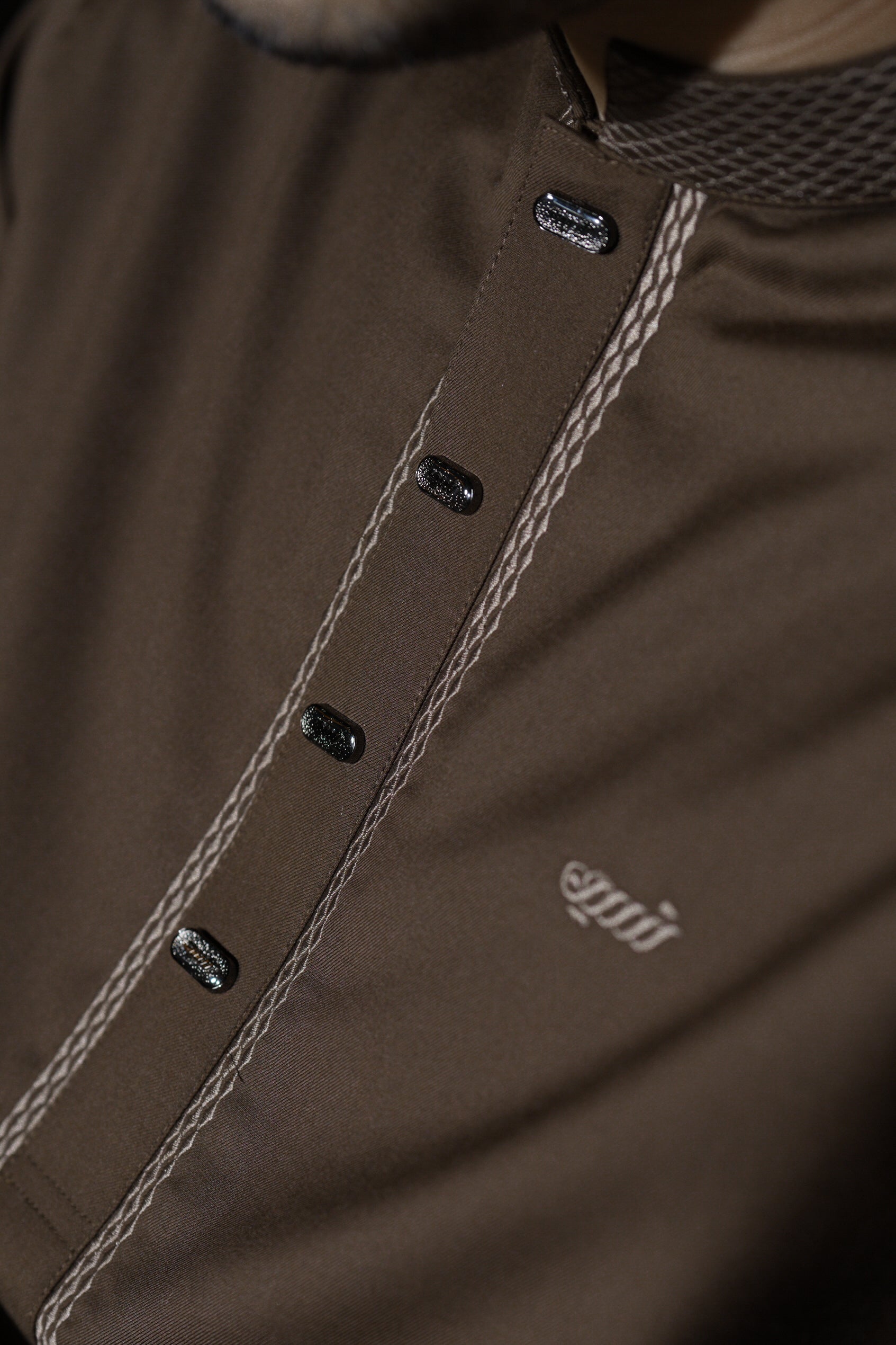 Close-up of a brown jacket with buttons and a brand logo.