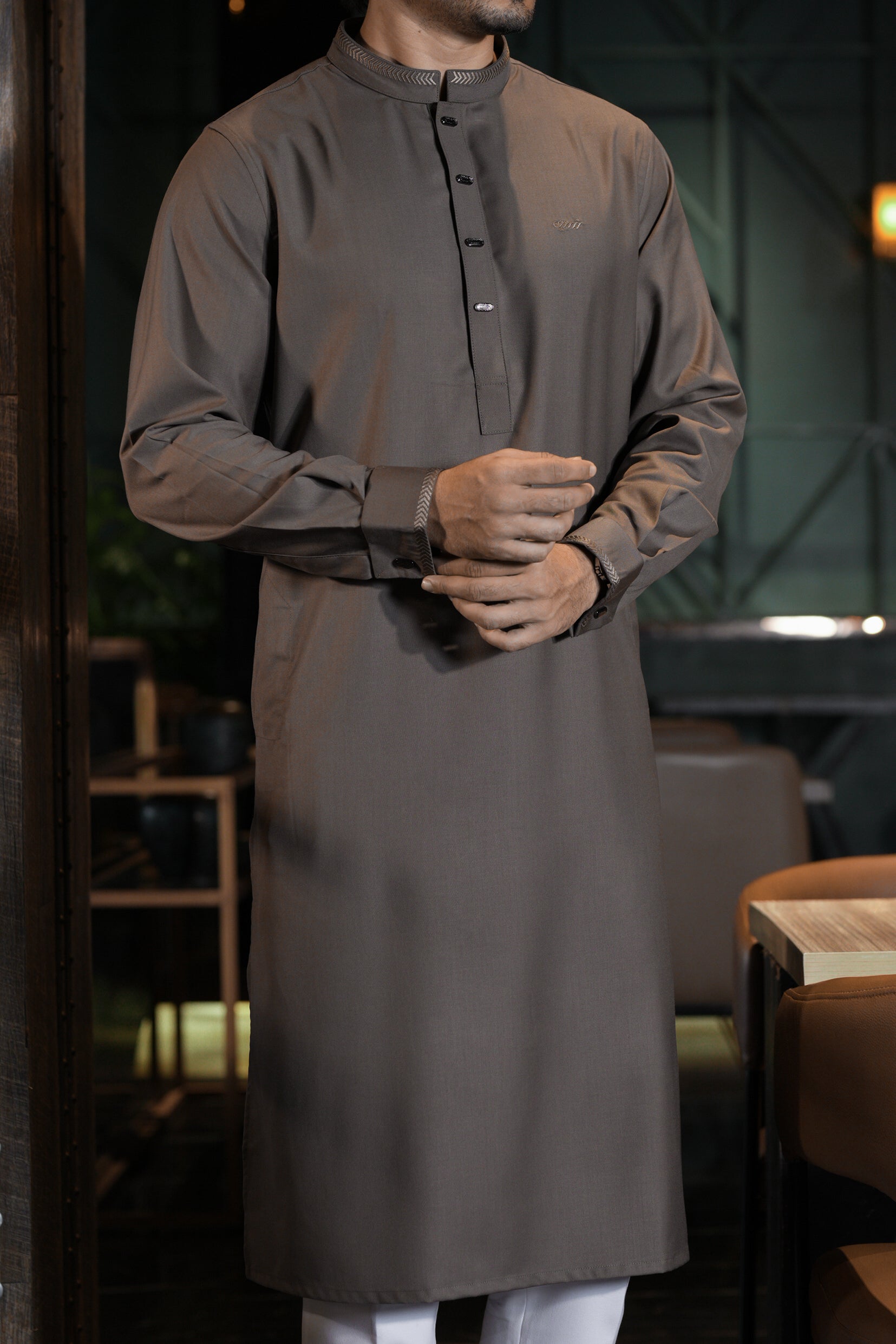 Man wearing a long dark gray traditional shirt in an indoor setting.
