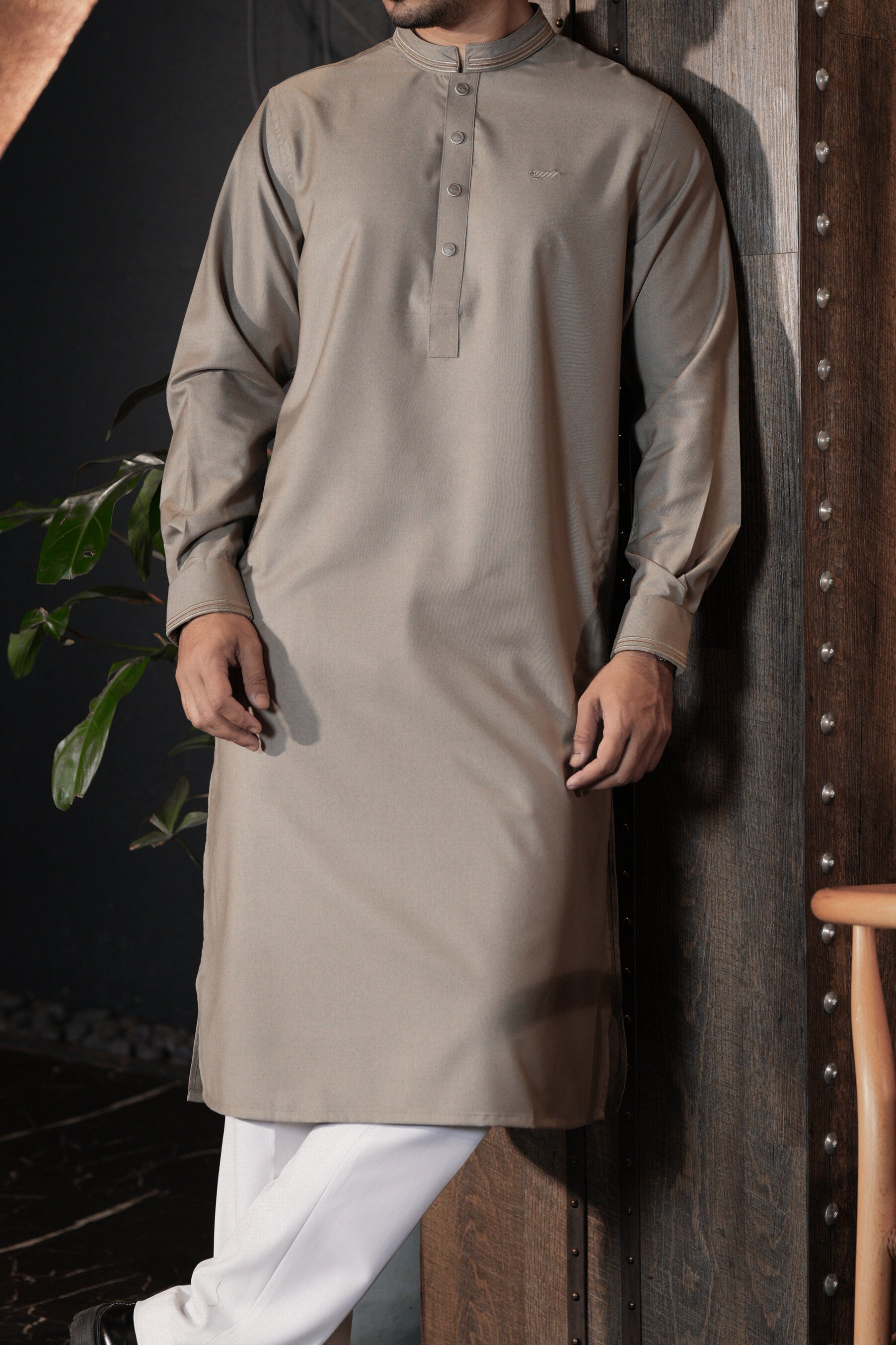Man wearing a beige kurta with white pants against a dark background